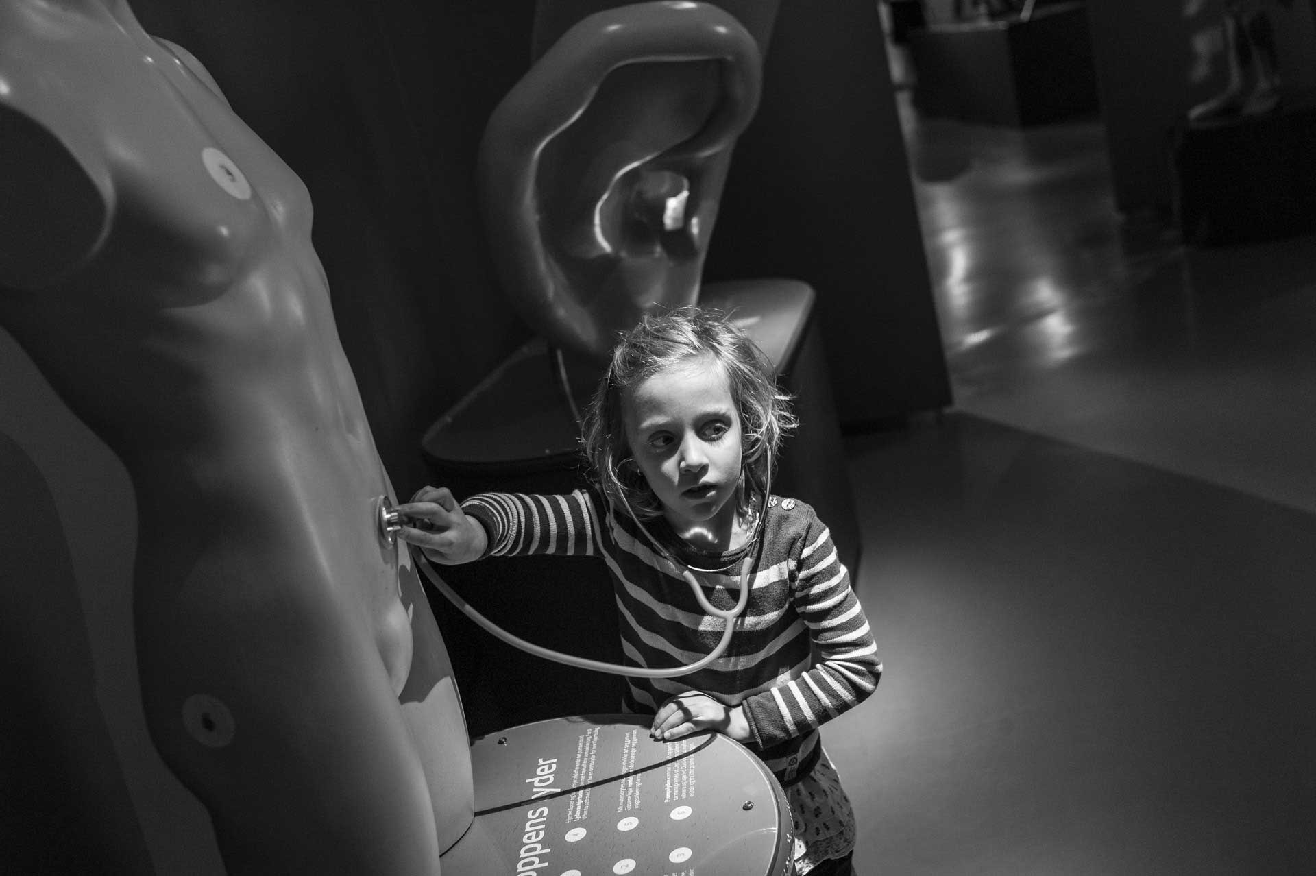 Malé dítě zkoumá model lidského těla stetoskopem v interaktivní expozici.